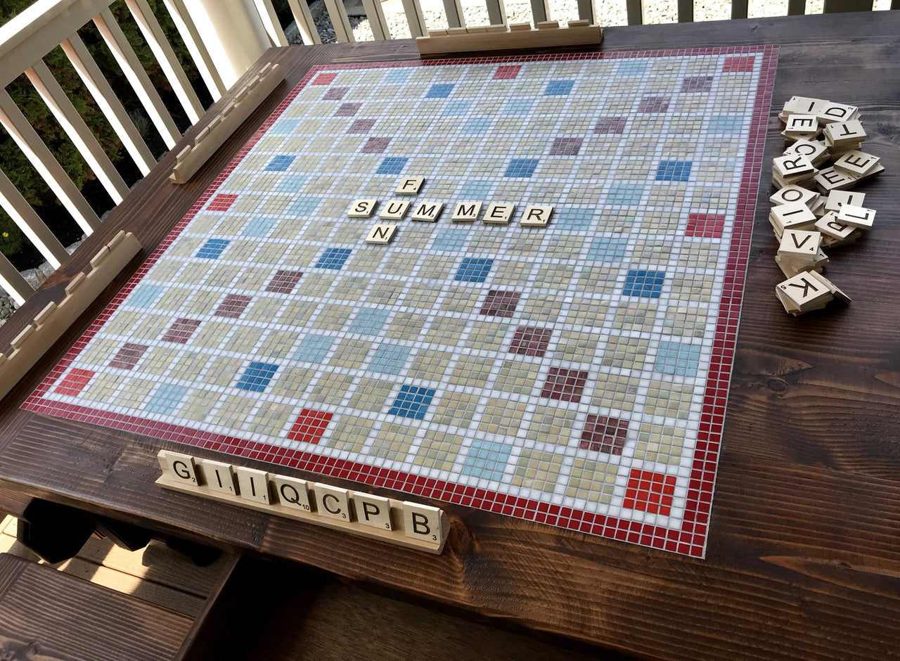 Close up view of inlaid tile Scrabble game and game pieces on oversized outdoor solid wood dining table.