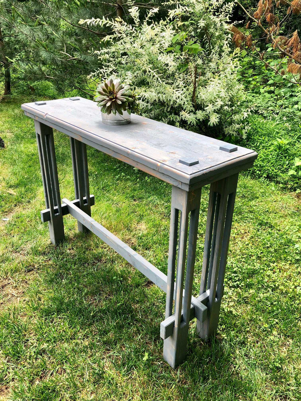 FSC-certified thermally modified solid wood outdoor bistro table with plant on top in quiet backyard with greenery all around.