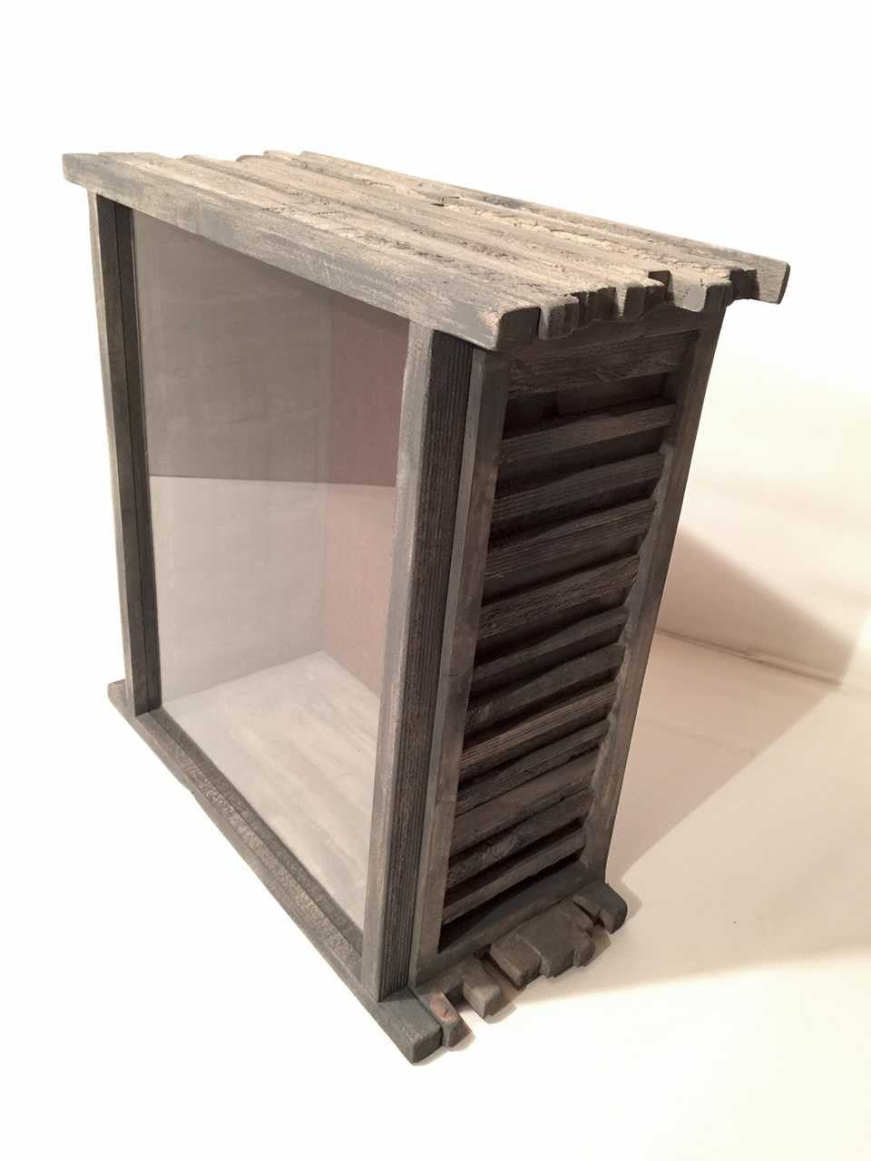 A  wooden display case with a shingled wood frame, clear glass window and burlap backing on white background